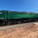 Class 93 tri-mode locomotive in racing green livery under a blue sky on rails with red earth in foreground