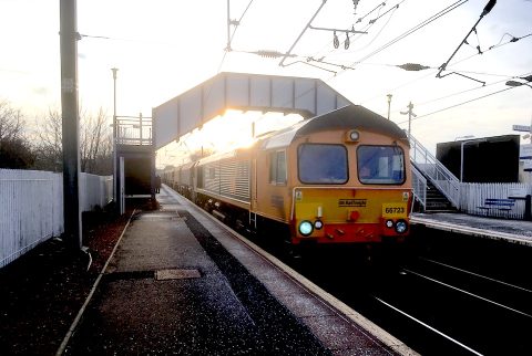 Freight train passing under footbridge with sunset in background