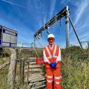 Proud engineer in orange safety suit standing in front of catinery wires