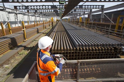 Orange saftey suited engineer inspects stockpile of new rails at British Steel works in UK