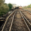 Track level image of damaged tracks with derailed wagons in background