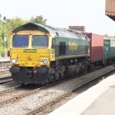 A Diesel hauled container train hurries through a small stain, as seen from the platform