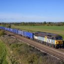 Class 56 diesel locomotive in a grey livery working a train of blue open wagons in a countryside setting